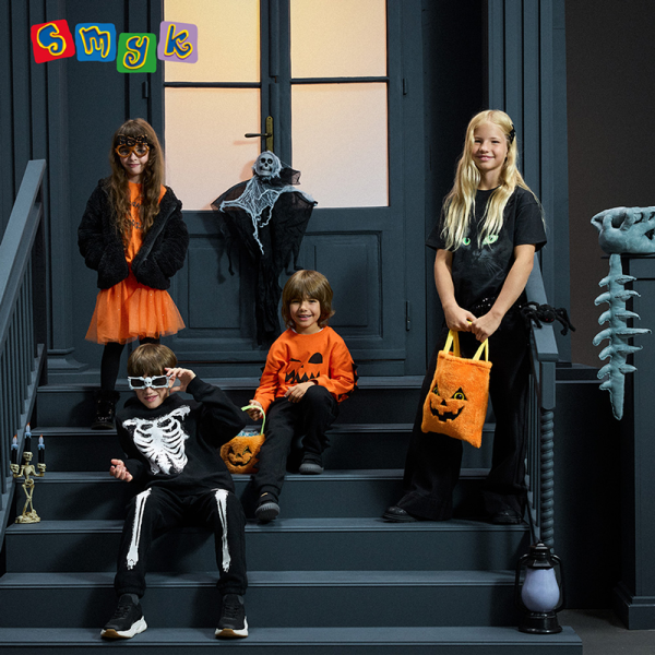 Grafika promująca przebrania na halloween w SMYKU dla dzieci. Czwórka dzieci przebrana w stroje halloweenowe na schodach przed domem.